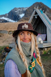 a blonde woman wearing a hat in front of a cabin