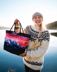 a woman holding a tote bag with mountains on it