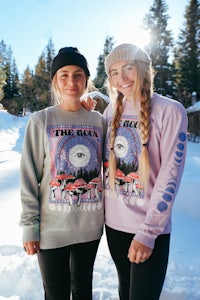 two women standing in the snow wearing sweatshirts